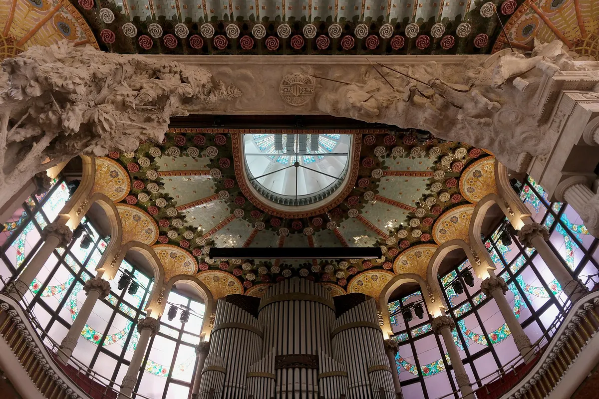 La mirada ascendente más allá del órgano hacia el arco sobre el escenario, con vidrieras a ambos lados y un techo de ornamentos dorados y de color.