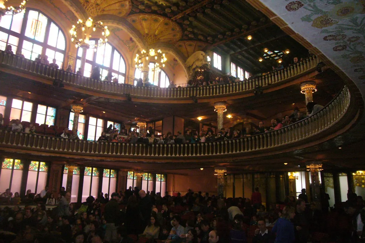 Der Konzertsaal des Palau, voller Menschen, mit Balkonen, Hängelampen und Bogenfenstern