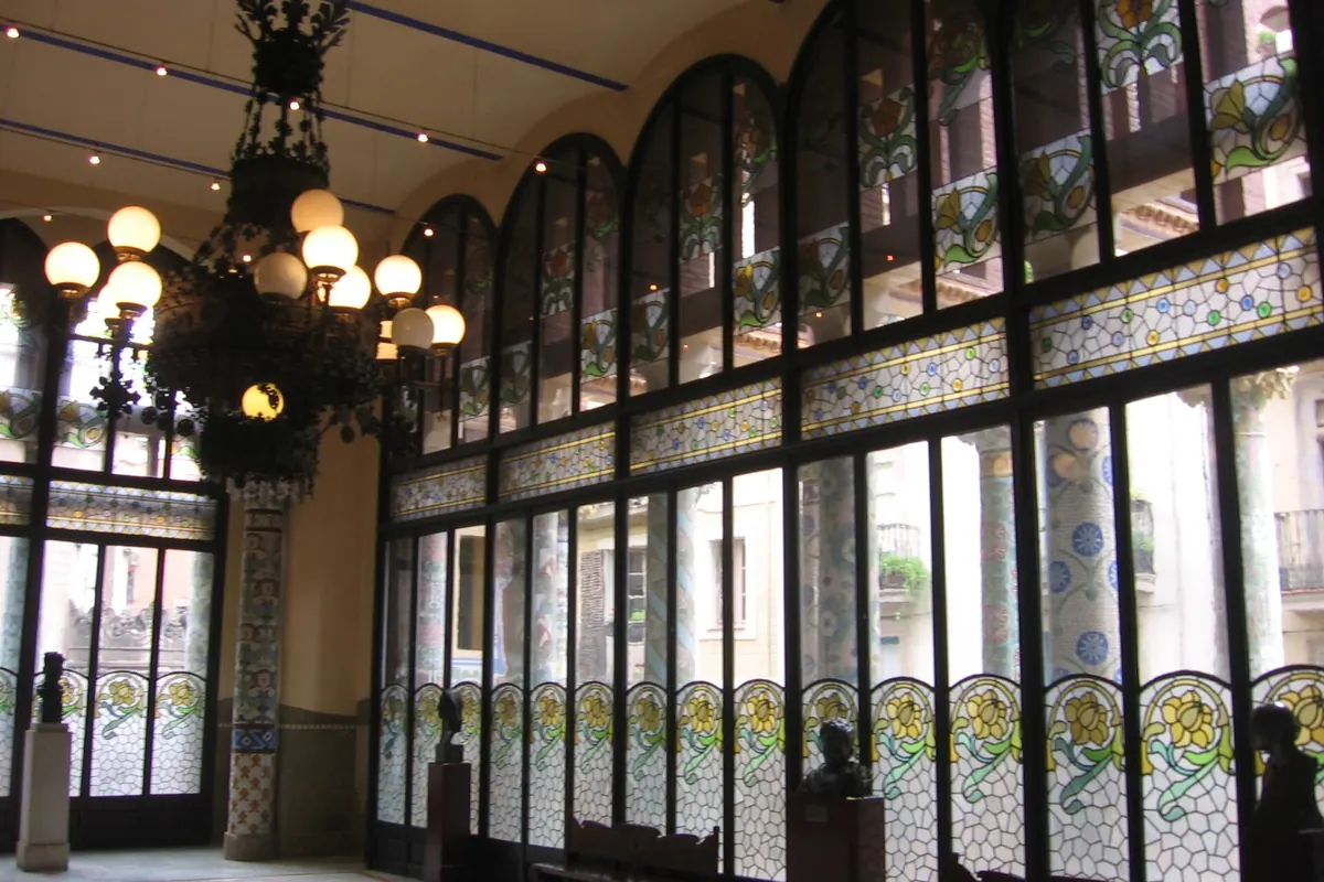 La Sala Lluís Millet, un salón alto con un muro de vidrieras arqueadas y una gran lámpara colgante.