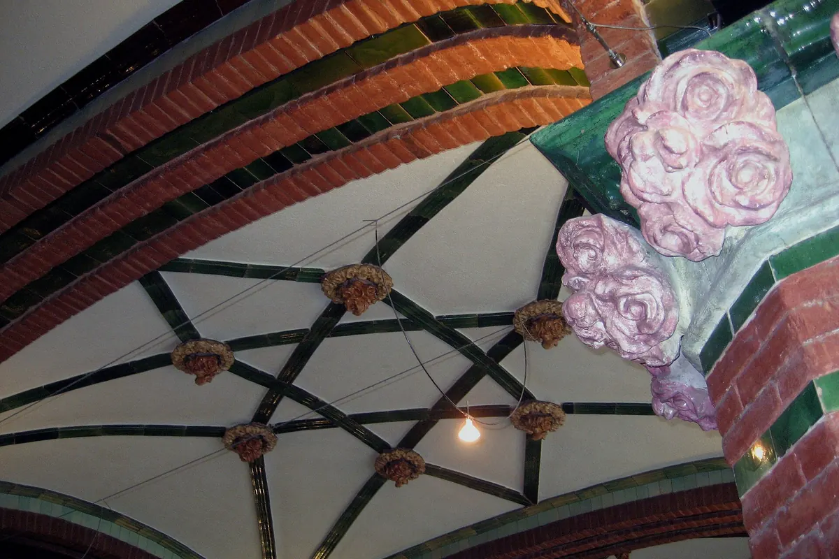 Una bóveda de ladrillo y azulejo verde en el Palau con una estrella de nervios de azulejo y rosas de cerámica rosa en la esquina.